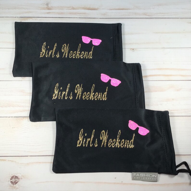 May include: Three black eyeglass cases with a gold glitter inscription that reads "Girls Weekend" and a pink glitter image of sunglasses. The bottom case has a small white tag that reads "FASHION COLLECTION".