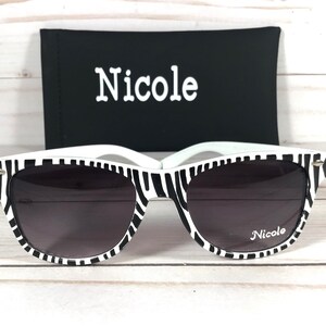 May include: Black and white zebra print sunglasses with a black case. The case has the word "Nicole" printed on it. The sunglasses also have the word "Nicole" printed on the right lens.