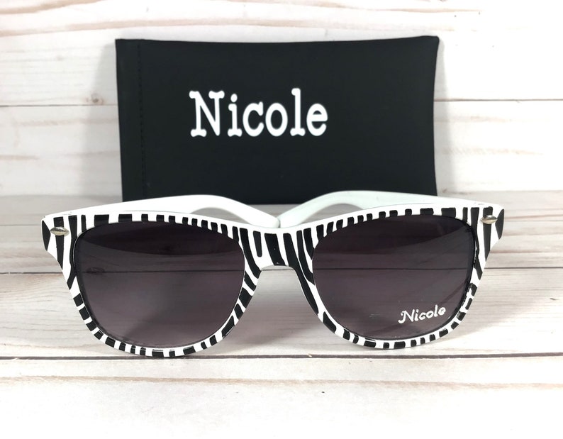 May include: Black and white zebra print sunglasses with a black case. The case has the word "Nicole" printed on it. The sunglasses also have the word "Nicole" printed on the right lens.