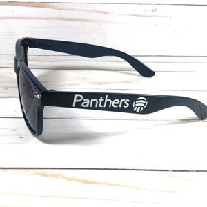 May include: Black sunglasses with a white "Panthers" logo and a white paw print on the side.