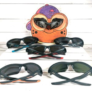 K&ouml;nnte beinhalten: F&uuml;nf Paar schwarze Sonnenbrillen mit verschiedenen farbigen Akzenten an den B&uuml;geln. Die Sonnenbrillen haben ein sportliches Design mit einem gebogenen Rahmen und schwarzen Gl&auml;sern.