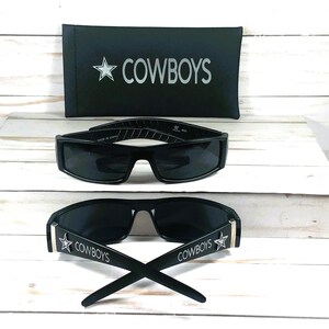 May include: Black sunglasses with the word "COWBOYS" and a star logo on the arms. A black case with the word "COWBOYS" and a star logo is also included. The sunglasses have a rectangular frame.