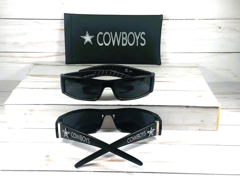 May include: Black sunglasses with the word "COWBOYS" and a star logo on the arms. A black case with the word "COWBOYS" and a star logo is also included. The sunglasses have a rectangular frame.