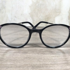Puede incluir: Gafas con montura negra y lentes redondas. Las monturas est&aacute;n adornadas con grupos de peque&ntilde;os pedrer&iacute;a rosa en las esquinas exteriores. Las gafas tienen un dise&ntilde;o cl&aacute;sico y elegante, adecuado para el uso diario.