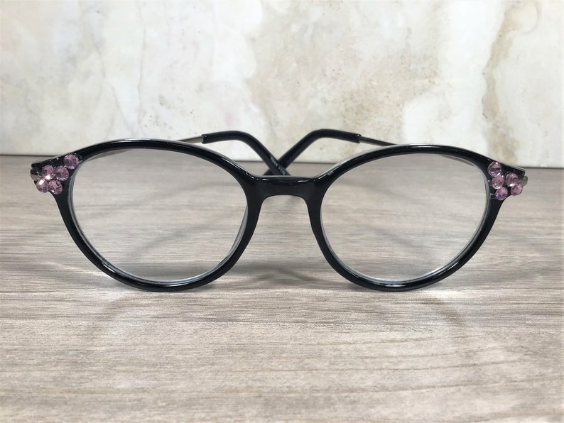 Puede incluir: Gafas con montura negra y lentes redondas. Las monturas est&aacute;n adornadas con grupos de peque&ntilde;os pedrer&iacute;a rosa en las esquinas exteriores. Las gafas tienen un dise&ntilde;o cl&aacute;sico y elegante, adecuado para el uso diario.