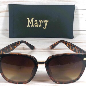 K&ouml;nnte beinhalten: Schildpatt-Sonnenbrille mit braunen Gl&auml;sern. Die Sonnenbrille befindet sich in einem schwarzen Etui mit dem Namen "Mary" darauf.