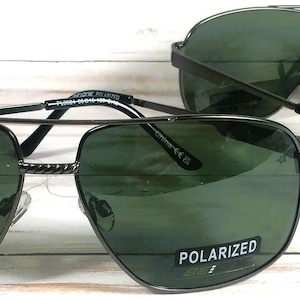 May include: Two pairs of black aviator sunglasses with green lenses. The sunglasses have a metal frame and polarized lenses. The text "POLARIZED" is printed on the right lens of the sunglasses in the foreground.