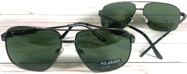 May include: Two pairs of black aviator sunglasses with green lenses. The sunglasses have a metal frame and polarized lenses. The text "POLARIZED" is printed on the right lens of the sunglasses in the foreground.