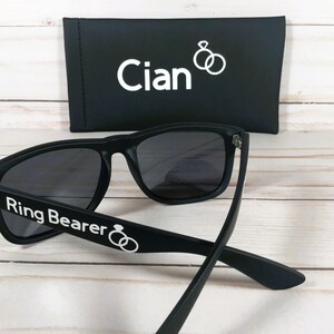 May include: Black sunglasses with the text "Ring Bearer" and two interlocking rings on the arm. The sunglasses come with a black case that has the name "Cian" and two interlocking rings printed on it.