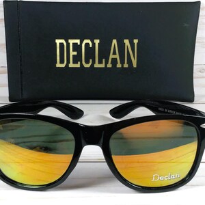 Pu&ograve; includere: Occhiali da sole neri con lenti a specchio arancioni. Gli occhiali hanno una montatura nera e il nome del marchio "Declan" &egrave; stampato sulla lente destra.
