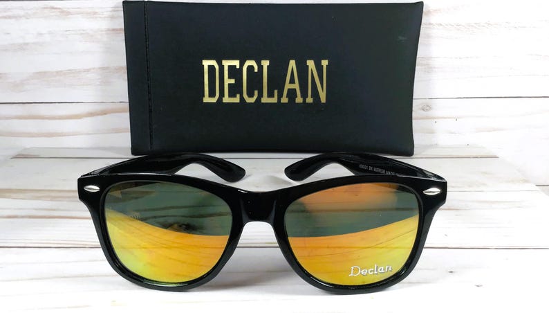 Pu&ograve; includere: Occhiali da sole neri con lenti a specchio arancioni. Gli occhiali hanno una montatura nera e il nome del marchio "Declan" &egrave; stampato sulla lente destra.