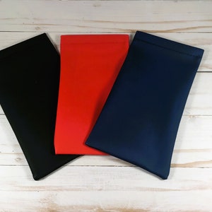 Op de afbeelding: Drie stoffen zakjes in zwart, rood en blauw. De zakjes zijn gemaakt van een zacht, glad materiaal en hebben een eenvoudige, rechthoekige vorm.