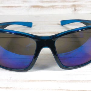 May include: Sport sunglasses with a dark teal frame and blue accents on the temples. The lenses have a mirrored finish with shades of blue and purple. The sunglasses are designed for outdoor activities.