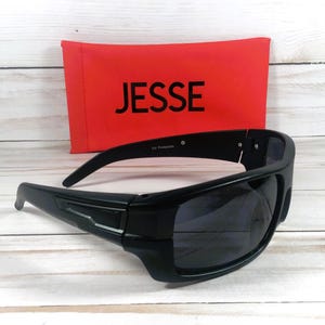 Pu&ograve; includere: Occhiali da sole neri avvolgenti con lenti scure. Un astuccio rosso con il nome "JESSE" in lettere bianche &egrave; dietro gli occhiali da sole. Gli occhiali da sole hanno "UV Protection" stampato sulla montatura.