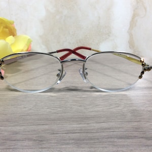 Puede incluir: Gafas de lectura con montura plateada y dise&ntilde;o de media montura. Las gafas tienen una patilla roja y dorada y est&aacute;n adornadas con detalles decorativos en los bordes exteriores. Las lentes son transparentes y la montura incluye el texto "8375 +2.75".
