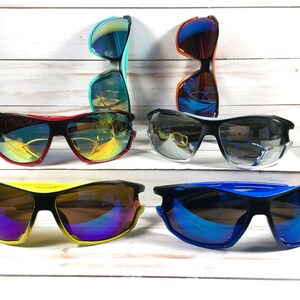 May include: Five pairs of sunglasses with different colored frames and lenses. The sunglasses have a sporty design with a wraparound style.