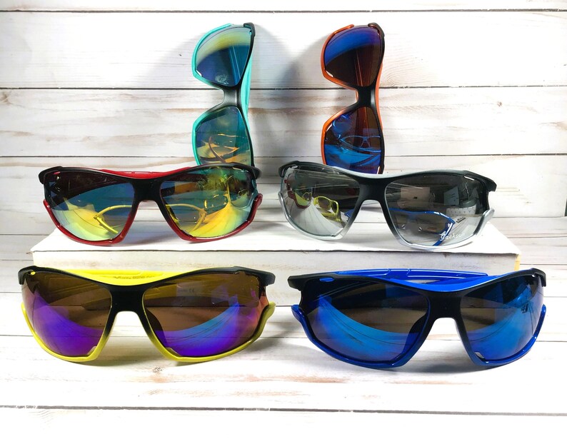 May include: Five pairs of sunglasses with different colored frames and lenses. The sunglasses have a sporty design with a wraparound style.