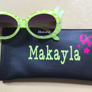 May include: Green polka dot sunglasses with a white bow on each side. The sunglasses come with a black case with the name Makayla written in green and a pink bow and star.