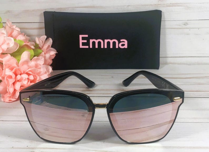 May include: Black sunglasses with rose gold mirrored lenses. The sunglasses are in a black case with the word "Emma" printed on it.