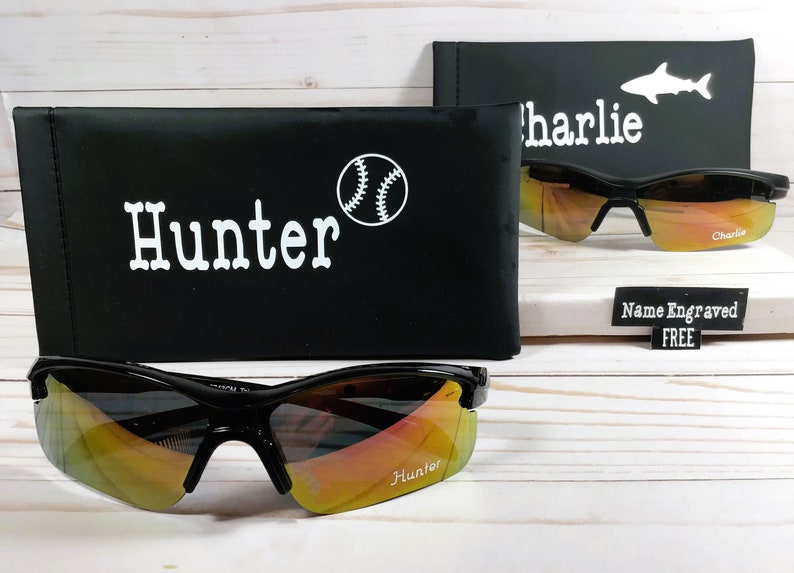 May include: Two pairs of black sunglasses with orange mirrored lenses. The sunglasses are in their cases, which are black with white text and a baseball graphic. The text on the cases reads "Hunter" and "Charlie".