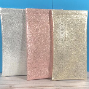 Pu&ograve; includere: Tre astucci rettangolari con una finitura testurizzata e scintillante. L'astuccio a sinistra &egrave; argento, quello centrale &egrave; oro rosa e quello a destra &egrave; oro. Ogni astuccio presenta un design sottile e verticale con un bordo superiore cucito.