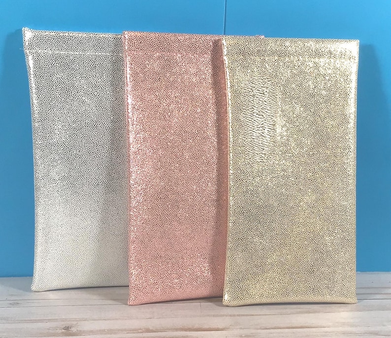 Pu&ograve; includere: Tre astucci rettangolari con una finitura testurizzata e scintillante. L'astuccio a sinistra &egrave; argento, quello centrale &egrave; oro rosa e quello a destra &egrave; oro. Ogni astuccio presenta un design sottile e verticale con un bordo superiore cucito.