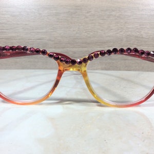 May include: Eyeglasses with a gradient frame, transitioning from red to yellow. The top of the frame is adorned with a row of purple rhinestones. The glasses have a cat-eye shape, suitable for various face shapes.