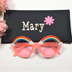 Puede incluir: Gafas de sol rosas con detalles de arco&iacute;ris y nubes. Las gafas de sol vienen con una funda negra que dice "Mary" con una flor rosa.