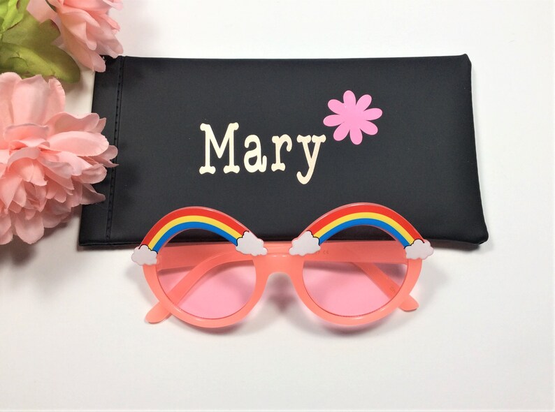 Puede incluir: Gafas de sol rosas con detalles de arco&iacute;ris y nubes. Las gafas de sol vienen con una funda negra que dice "Mary" con una flor rosa.
