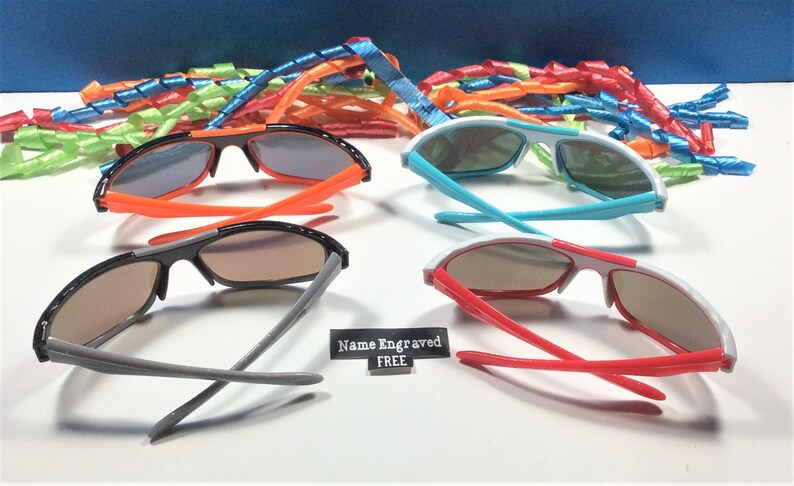Peut inclure: Quatre paires de lunettes de soleil avec des montures et des verres de couleurs diff&eacute;rentes. Les montures sont noires, orange, blanches et rouges. Les verres sont tous de couleur brun fonc&eacute;. Le texte "Nom grav&eacute; GRATUIT" est visible sur l'image.