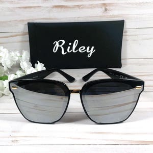 May include: Black sunglasses with a silver mirrored lens and a black case with the name "Riley" printed in white.