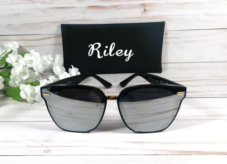 May include: Black sunglasses with a silver mirrored lens and a black case with the name "Riley" printed in white.