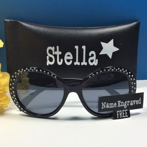 May include: Black sunglasses with a rhinestone trim and a black case with the name "Stella" and a star printed on it. The sunglasses come with a free name engraving.