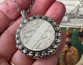 May include: A silver locket necklace with a detailed engraved design. The locket has a beaded border and is attached to a delicate silver chain.