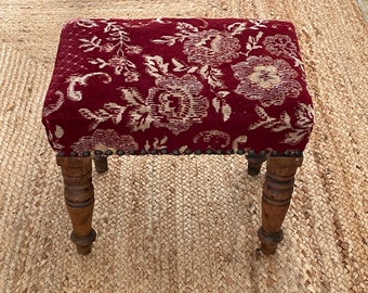 May include: A small red and white floral patterned stool with turned wooden legs.
