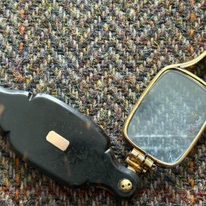 Op de afbeelding: Een antieke opvouwbare vergrootglas met een schildpad handvat en een goudkleurig frame. De rechthoekige lens is geplaatst in een scharnierend frame en de handgreep heeft een decoratief ontwerp. Het vergrootglas is open en toont de lens.