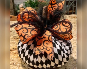 May include: A black and white checkered pumpkin with an orange and black ribbon bow. The bow has a swirl pattern and is tied with a black feather.