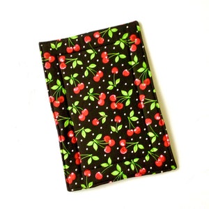May include: A black fabric placemat with a cherry print and white polka dots. The placemat has a white border.