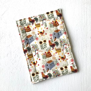 May include: A white cotton kitchen pot holder with a colorful pattern of roosters, houses, sunflowers, and other floral elements.