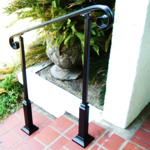 May include: Black metal handrail with decorative scrollwork on the ends. The handrail is mounted to two black metal posts with square bases. The handrail is installed on a set of stairs.