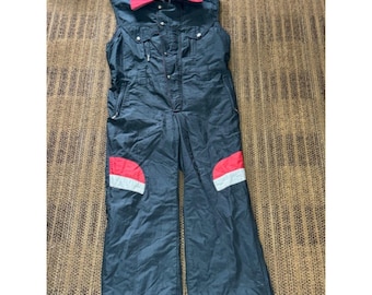 May include: A sleeveless black jumpsuit featuring a bright red fold-down collar, a front button closure, and two chest pockets. The legs include red and white horizontal accent panels on the thighs, providing a distinct contrast to the dark fabric.