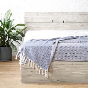 May include: A white bed with a blue and white patterned throw blanket. The bed has a wooden headboard and footboard. A wooden paddle is hanging on the wall behind the bed.