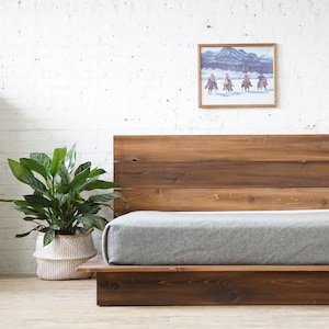 May include: A wooden platform bed frame with a grey mattress and a headboard made of reclaimed wood planks. The bed is in a room with white brick walls and a framed picture above the headboard.