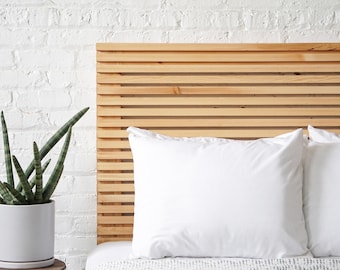 May include: A wooden headboard with a slatted design, featuring two white pillows on a bed with a white and gray patterned bedspread.
