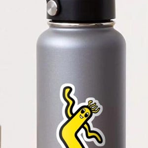 May include: A gray water bottle with a black handle and lid. A yellow cartoon character with black outlines is featured on the bottle. The character has a smiling face and wavy arms and legs.
