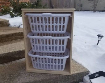 Puede incluir: Un cesto de ropa de madera de tres niveles con cestas de plástico blanco. El cesto está sobre un conjunto de escalones de concreto cubiertos de nieve.