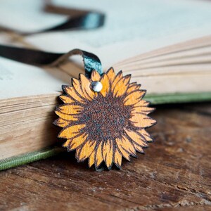 May include: A wooden sunflower bookmark with a black ribbon attached. The bookmark is lying on top of a closed book.