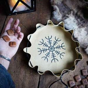 May include: A leather tray with a Vegvisir symbol in black on a white background. The tray is surrounded by brown wooden runes.