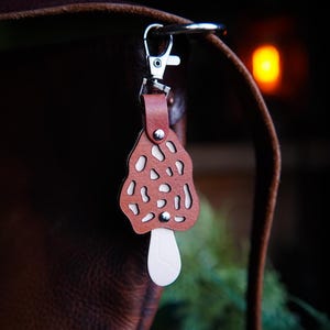 May include: A brown leather mushroom-shaped keychain with a white stem attached to a silver key ring.