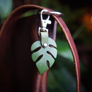 May include: A green leather monstera leaf keyring attached to a brown leather strap.